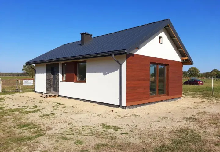 Nowy dom szkieletowy na zgłoszenie, z białym tynkiem i drewnianą elewacją, gotowy do zamieszkania.