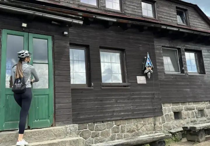 Kobieta w kasku rowerowym zbliża się do drzwi schroniska Chatka Górzystów.