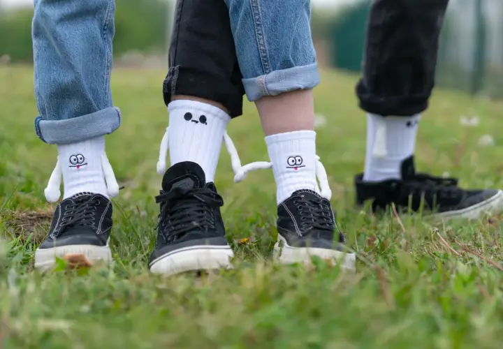 Jak nosić długie skarpety? Zabawne białe skarpety z postaciami i czarne trampki na trawie.