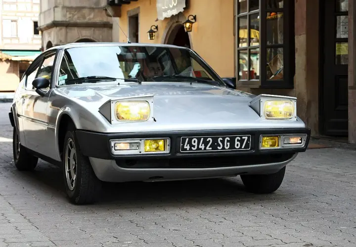 Silberner Simca Bagheera mit ausklappbaren Scheinwerfern fährt durch eine Gasse mit Kopfsteinpflaster.