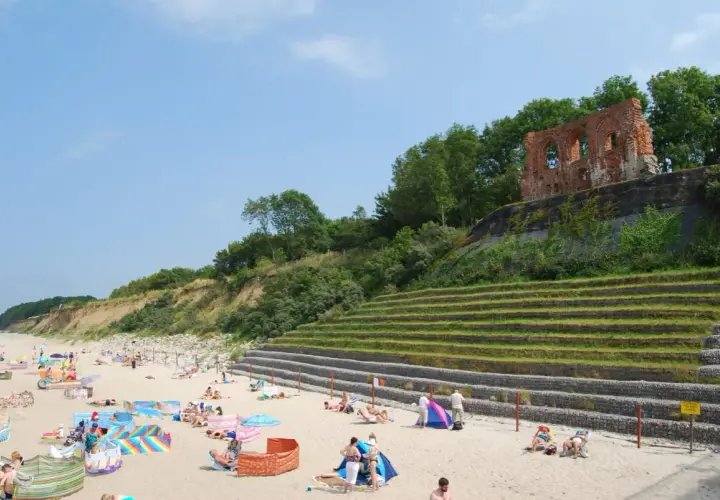 Plaża w Rewalu z ruinami na klifie. Ludzie odpoczywają na piasku, ciesząc się słońcem i widokiem. To popularne rewal atrakcje.