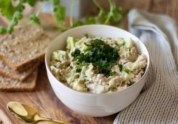 Pyszna pasta z awokado i tuńczyka, udekorowana natką pietruszki, podana z chlebem.