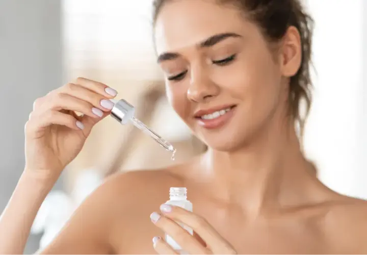 Kobieta z uśmiechem aplikuje serum do twarzy. Czy serum do twarzy można stosować codziennie? Tak, dla pięknej i zdrowej skóry.