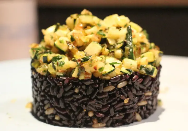 Riso nero compattato a cilindro, guarnito con un'abbondante porzione di zucchine saltate e erbe aromatiche.