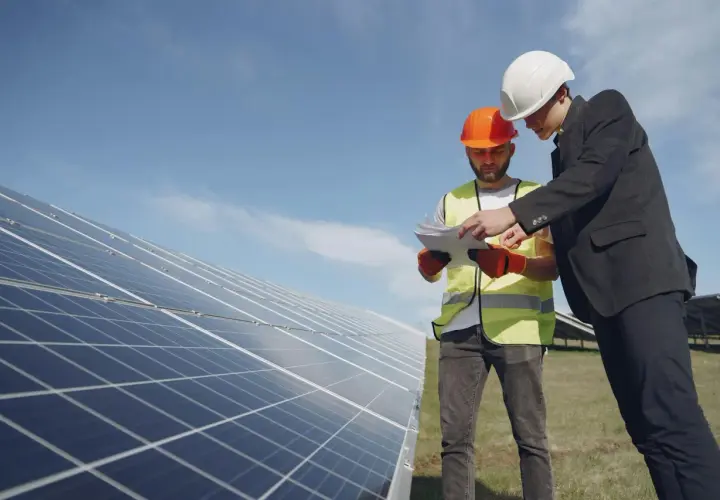 Deux hommes en casque discutent des plans près de panneaux solaires, en vue du remplacement d'un appareil sous garantie.