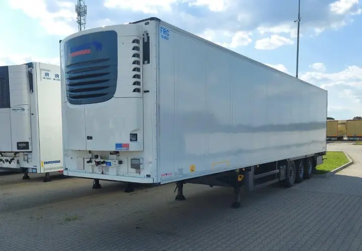 Biała naczepa chłodnia Schmitz Cargobull z niebieskim logo, zaparkowana na zewnątrz.