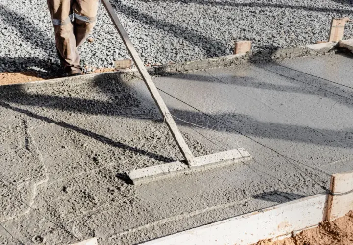 Un ouvrier lisse une **pente en béton** fraîchement coulée avec un râteau, créant une surface lisse pour une nouvelle construction.