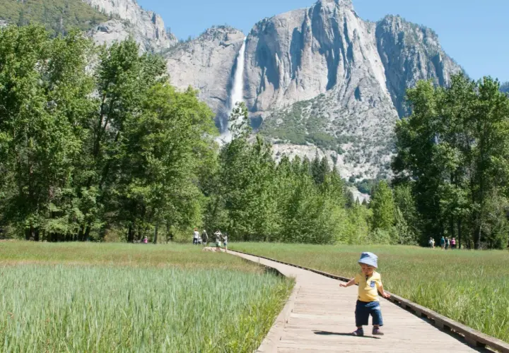Mały chłopiec na ścieżce w Yosemite, w tle wodospad i trzy korony gór.