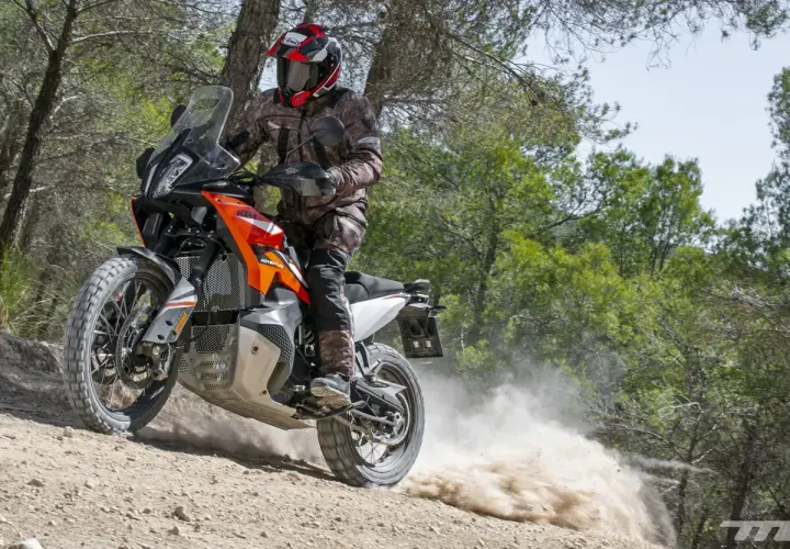 Motociclista con casco y equipo de aventura, derrapando una KTM 490 Adventure en un camino de tierra con polvo levantándose.