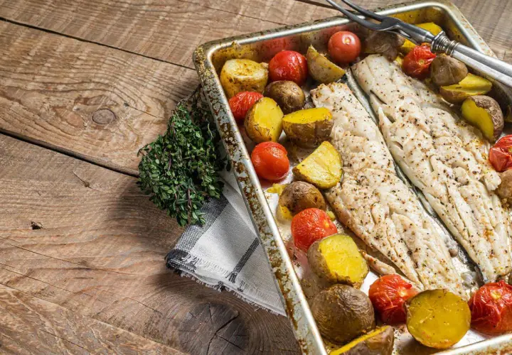 Coda di rospo al forno con patate e pomodorini su un tagliere di legno rustico, guarnita con timo fresco.