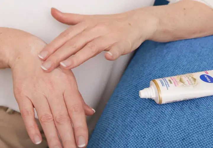 Mani che si applicano crema, forse per alleviare il prurito avambracci cause. Tubetto Nivea in primo piano.