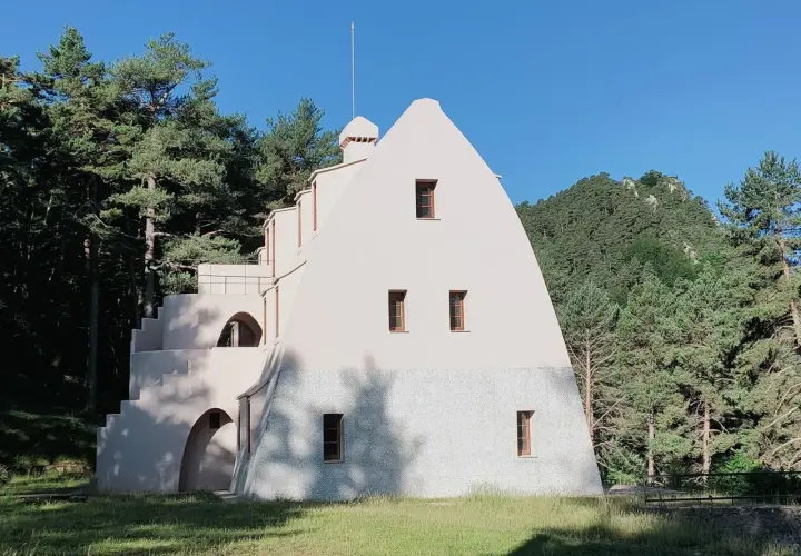 Edificio singular en la Serra de Catllaras, rodeado de pinos y con un cielo azul intenso.