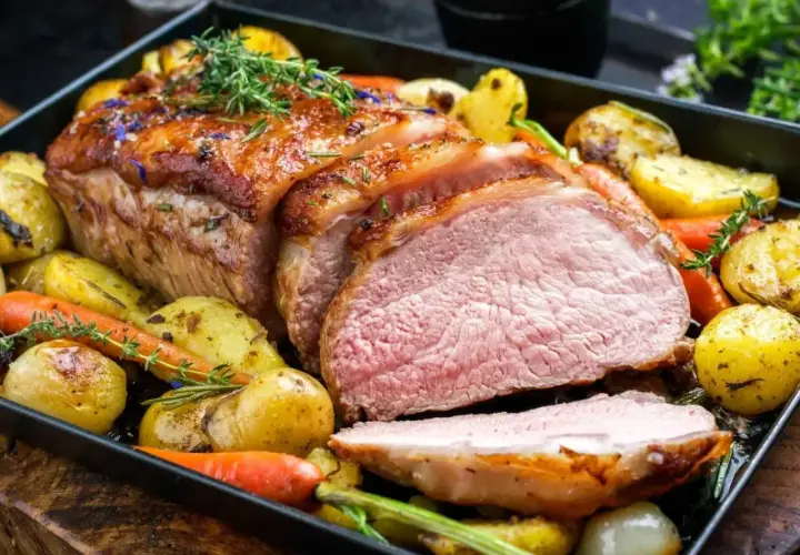 Soczysta polędwiczka wieprzowa pieczona z ziemniakami i marchewką, udekorowana ziołami.