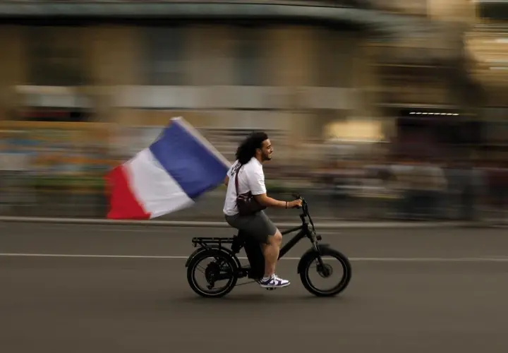 Uomo in bici sfreccia con bandiera francese, un'immagine che sfugge alle recensioni sull'odio.