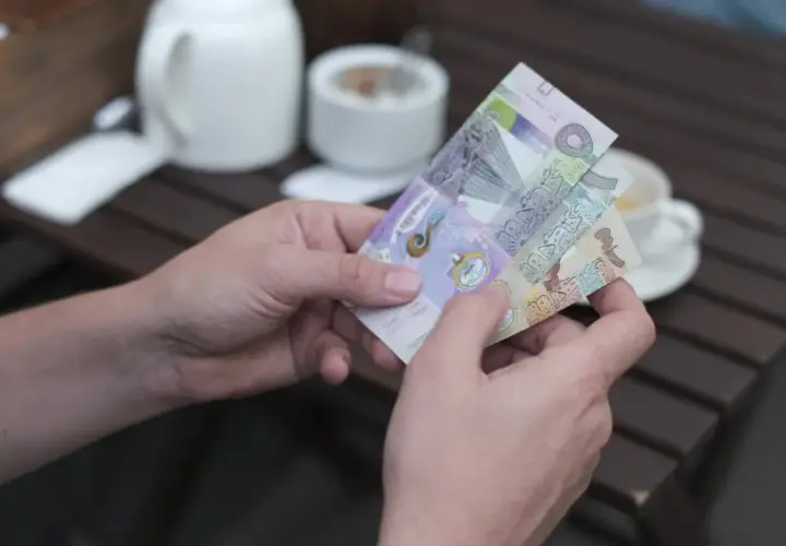Dłonie trzymają banknoty, które mogą być najdroższą walutą świata. W tle biały czajniczek i filiżanka kawy.