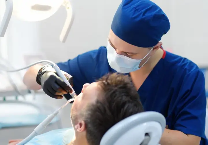 Dentysta w masce i rękawiczkach wykonuje zabieg. Sen o dentystach może oznaczać troskę o zdrowie lub potrzebę zmian.