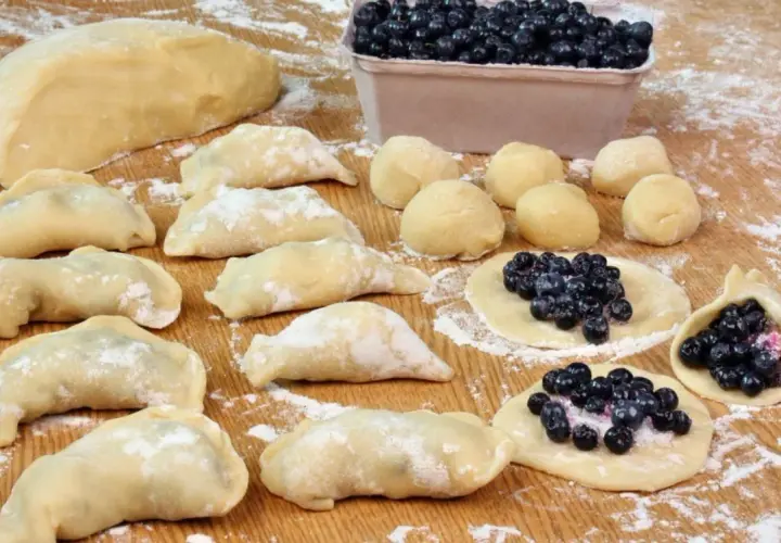 Przygotowania do tego, jak zrobić pierogi z jagodami: ciasto, kulki ciasta, gotowe pierogi i te w trakcie lepienia z jagodami.