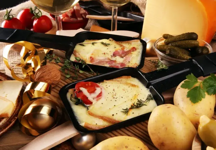Comment présenter une raclette : fromage fondu, pommes de terre, cornichons et charcuterie, le tout prêt à être dégusté.
