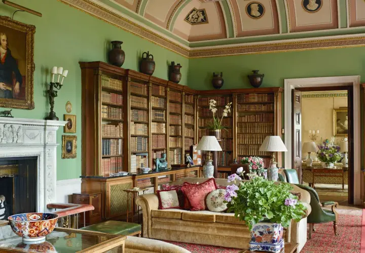 A cozy library with floor-to-ceiling bookshelves, a fireplace, and plush seating, embodying a classic countryside style.
