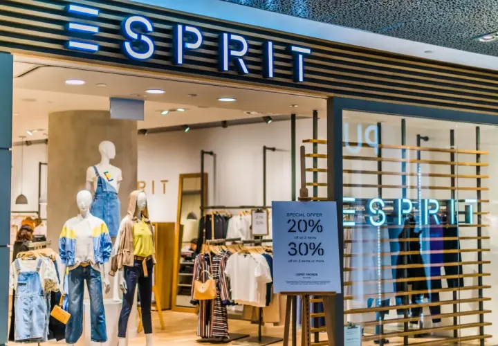Sklep Esprit z neonowym logo. Manekiny prezentują letnie ubrania, a obok widoczna jest tablica z promocją.