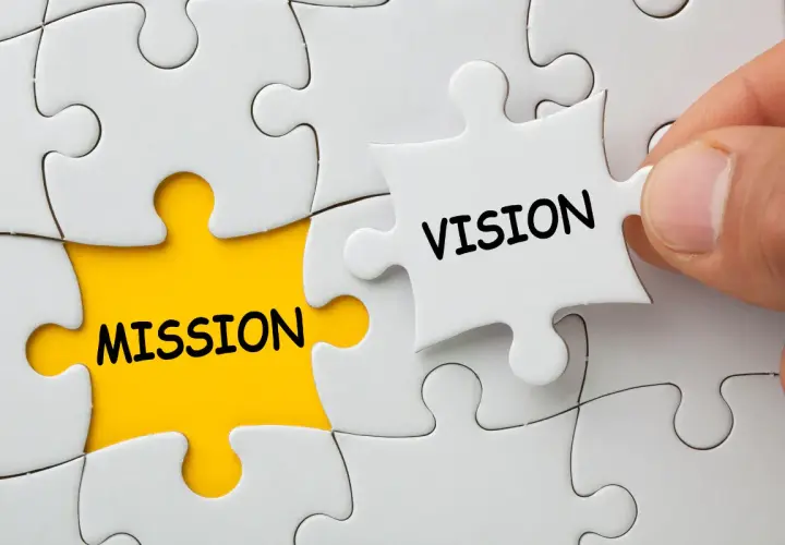 Dłoń dopasowuje element układanki z napisem "VISION" do pola z napisem "MISSION", symbolizując wizję firmy.