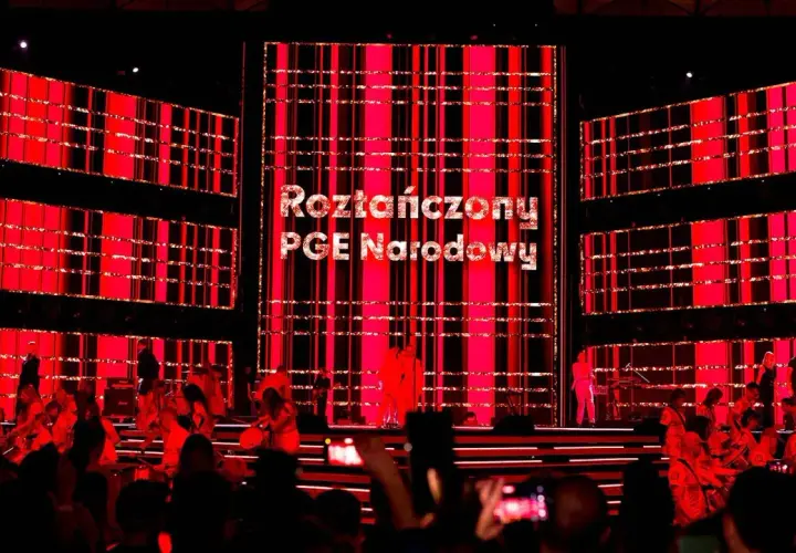 Roztańczony PGE Narodowy rozświetlony czerwienią. Na scenie artyści, w tle wielkie ekrany z napisem.