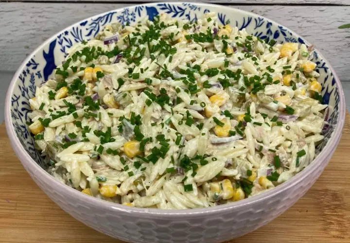 Pyszna sałatka z tuńczykiem i makaronem orzo, z kukurydzą i szczypiorkiem, w ozdobnej misce.