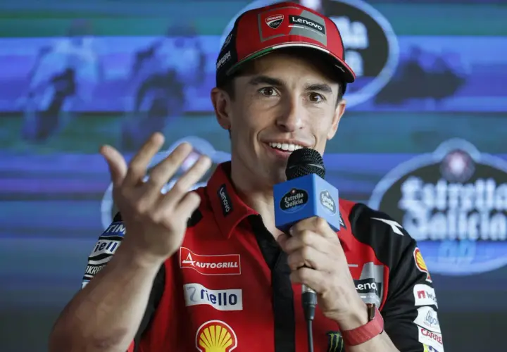 Marc Márquez, con su gorra roja y polo de Ducati, habla con un micrófono. Su edad se refleja en su energía y sonrisa.