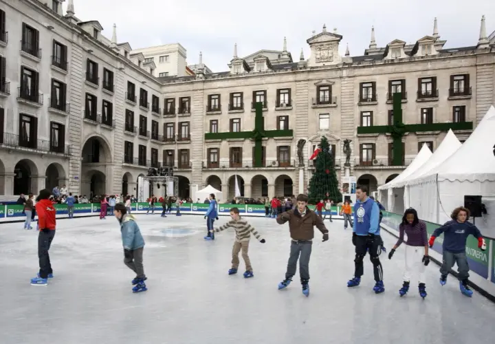 Gente patinando en la pista de hielo de Santander, con un árbol de Navidad y edificios históricos de fondo.