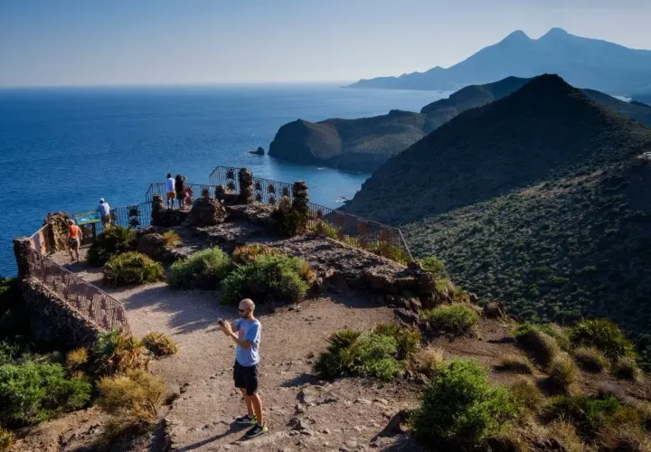 Un hombre toma una foto en un mirador con vistas a la cala de enmedio y montañas.