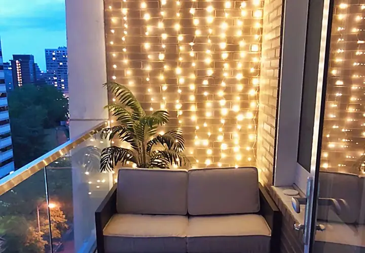 Ciepłe światła tworzą przytulny pomysł na oświetlenie balkonu. Sofa i palma dodają uroku.
