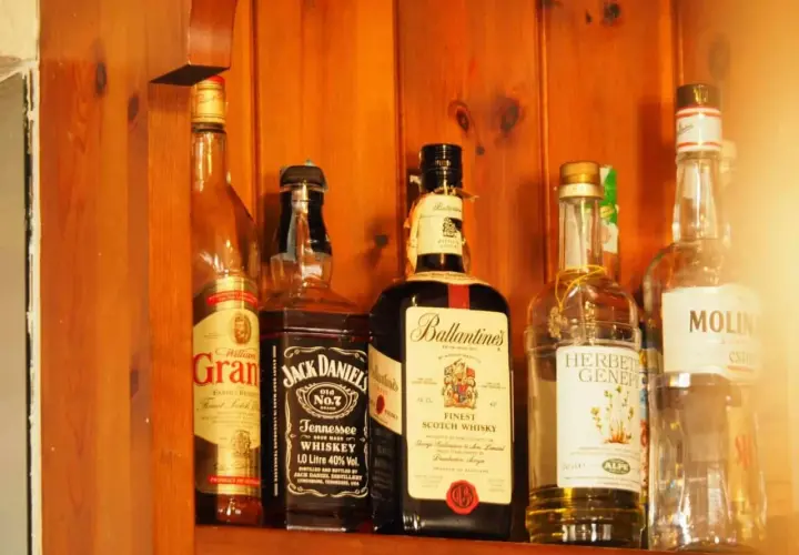 Butelki whisky na drewnianej półce. Zwróć uwagę na zmętnienie i osad w starych butelkach, by rozpoznać objawy zepsutej whisky.