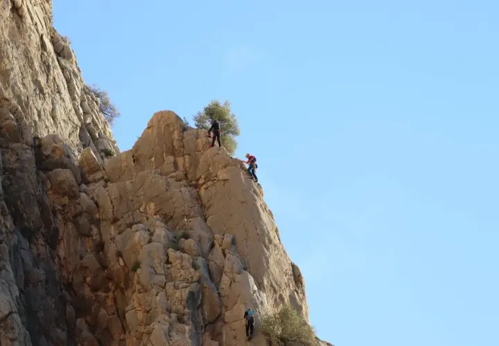 Tres escaladores desafían el chorro escalada en una pared rocosa bajo un cielo azul.