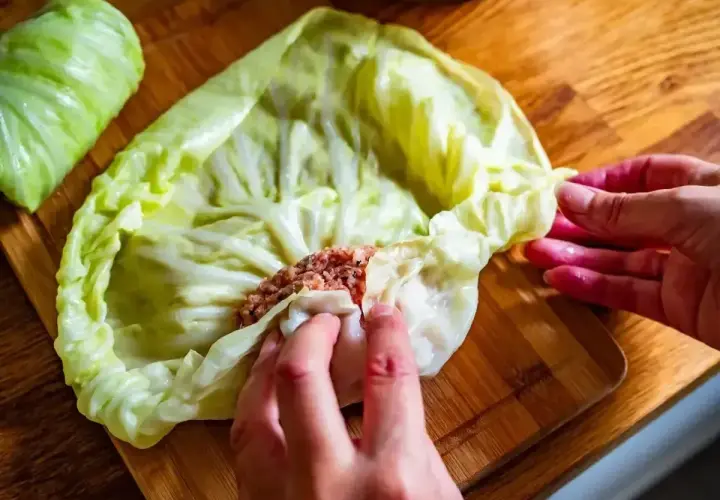 Ręce zwijają liść kapusty z farszem mięsnym. To początek przygotowań do pysznego dania, idealnego na przepis na gołąbki na 1kg mięsa.