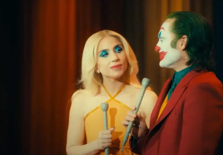 La femme du Joker, avec son maquillage bleu scintillant, semble chanter face à lui, le clown au visage blanc et rouge.