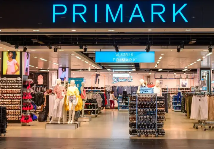 Wejście do sklepu Primark w Polsce. Widać neonowy napis "PRIMARK" i wystawione ubrania na manekinach i wieszakach.