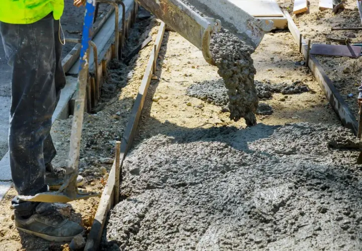 Betoniarka wylewa beton na plac budowy. Pracownik w kamizelce i spodniach przygotowuje teren. Zastanawiasz się, ile kosztuje kubik betonu?