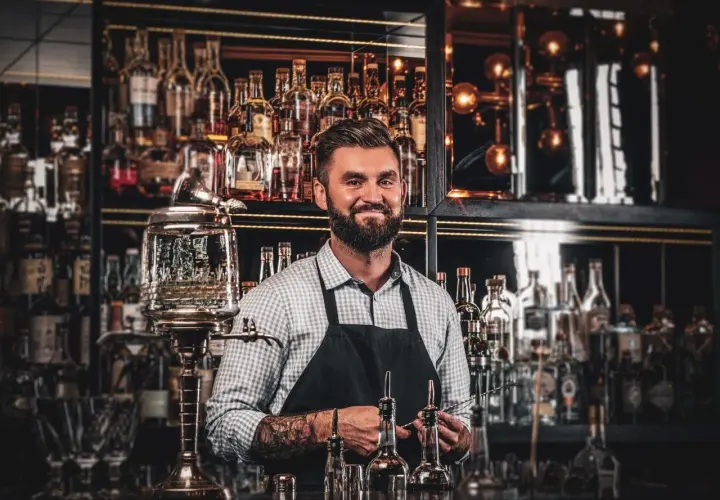 Barman z tatuażami prezentuje akcesoria do przygotowania absyntu. Poznaj tajniki, jak pić absynt, by w pełni docenić jego smak.