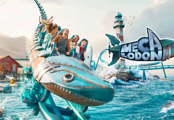 Un train de montagnes russes en forme de requin mécanique sur l'eau, avec un phare et un village de pêcheurs.