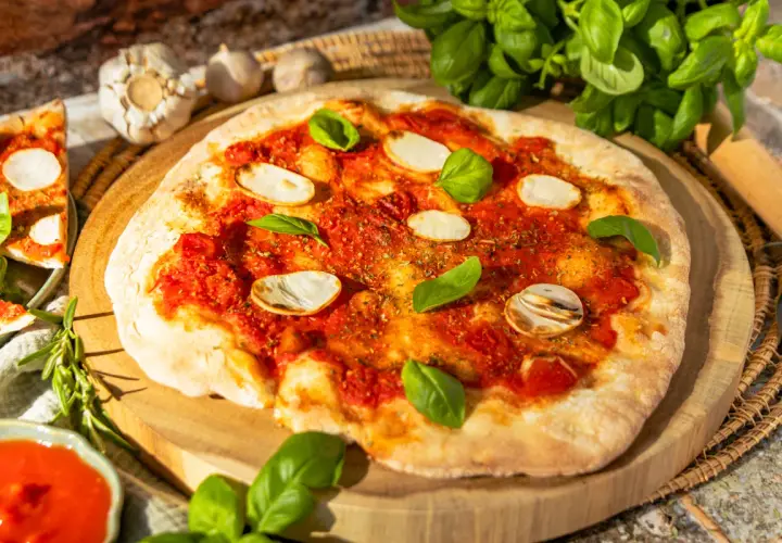 Eine köstliche Pizza Marinara mit Tomatensauce, Knoblauchscheiben und frischem Basilikum auf einem Holzbrett.