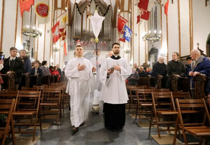 Liturgia Wielkiego Czwartku w kościele. Dwóch ministrantów w białych szatach niesie kadzidło i chorągiew.