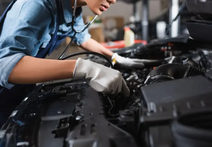Mechanik w rękawiczkach bada silnik, szukając uszkodzonej pompy wody i jej objawów.