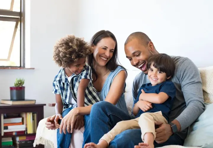 Famille souriante sur un canapé, profitant d'un moment de joie. Ce bonheur est rendu possible grâce à un **prêt conventionné** qui leur a permis d'acquérir leur foyer.