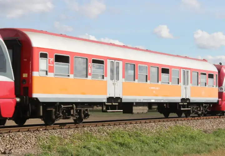 Lekki wagon pasażerski w kolorach pomarańczowo-białym i czerwonym jedzie po torach.