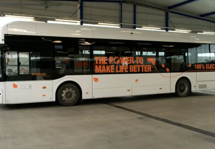 Ein weißer, moderner elektrischer Bus steht in einer Halle. Auf der Seite steht "THE POWER TO MAKE LIFE BETTER" und "100% ELECT".