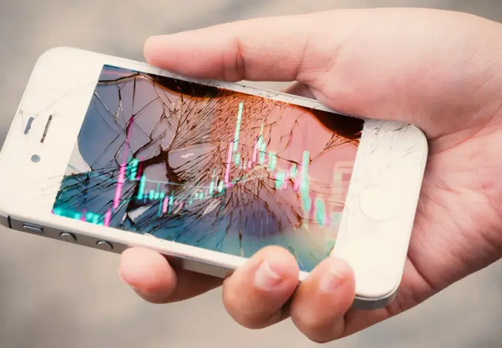 Dłoń trzyma pęknięty smartfon z wykresem giełdowym. Ubezpieczenie ekranu to spokój ducha.
