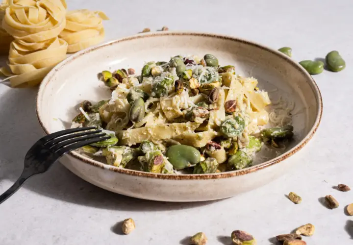 Makaron tagliatelle z bobem i pistacjami, posypany parmezanem, na talerzu.