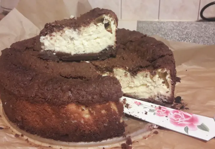 Pyszny sernik królewski bezglutenowy z czekoladową kruszonką i kremowym nadzieniem. Pokrojony kawałek czeka na spróbowanie.