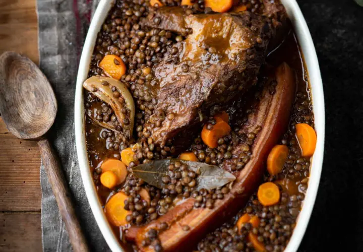 Un plat réconfortant de petit salé aux lentilles, avec des morceaux de viande savoureux, des carottes et des oignons, prêt à être servi.