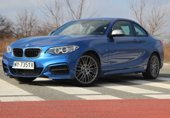 Niebieskie BMW 235i na pasach. Sportowy samochód z charakterystycznym grillem i felgami.
